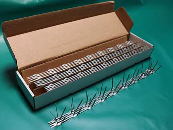 A box containing strips of metallic bird spikes on a green surface.