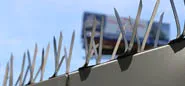 Bird spikes atop a wall, with a blurry billboard in the background under a clear sky